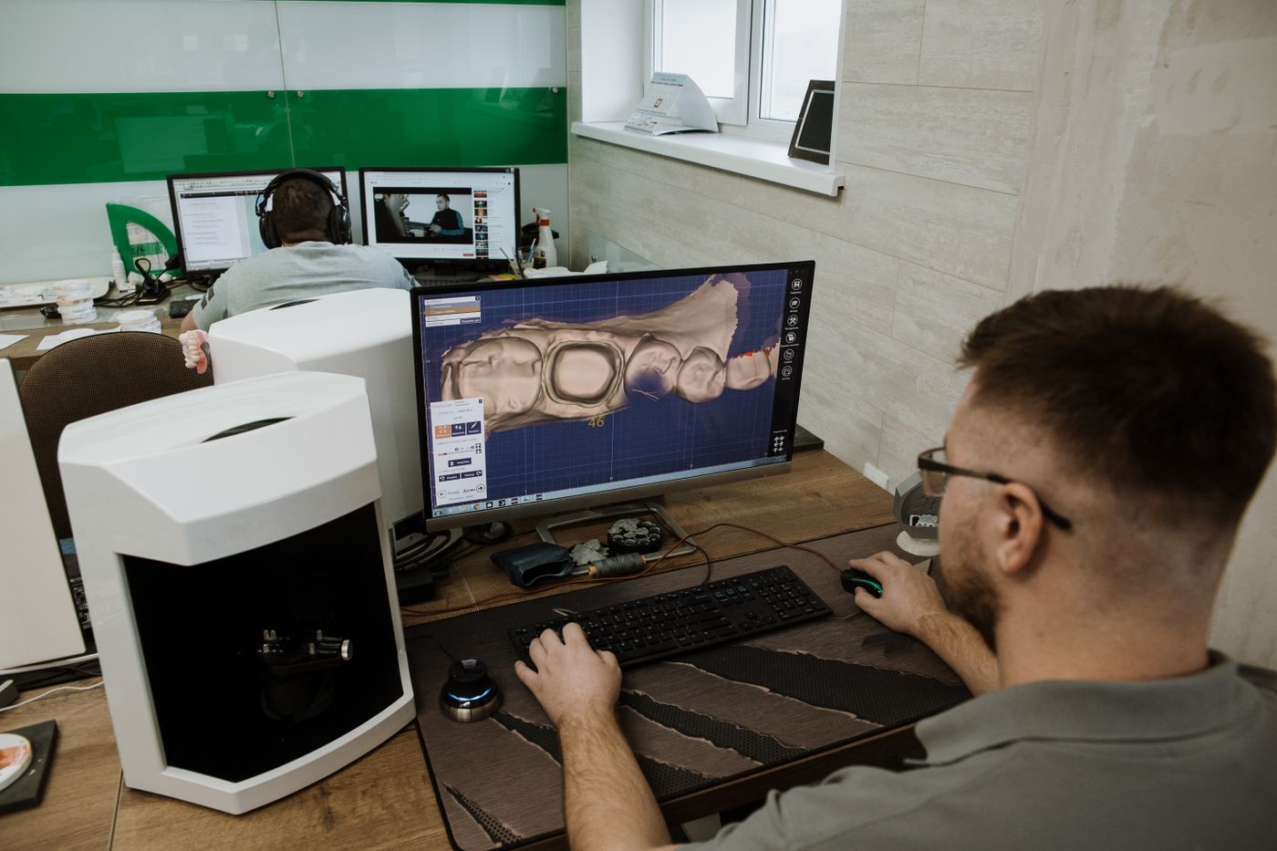Zahntechniker konstruiert eine Krone am CAD-Arbeitsplatz neben einem Laborscanner